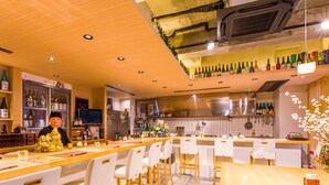 A restaurant with a long counter, white chairs, and a variety of bottles on shelves. - Mr.KINJO in MATSUYAMA (Naha)