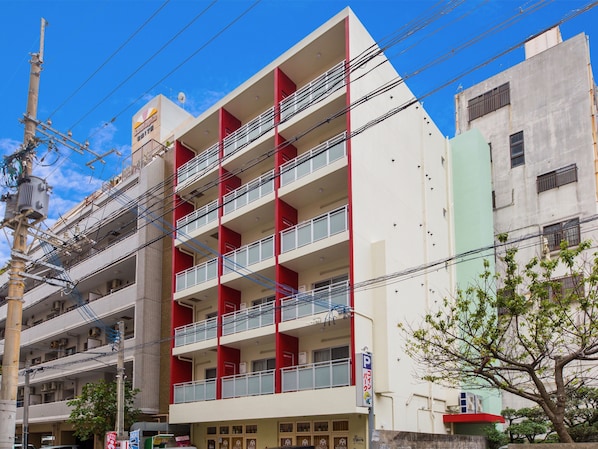 Un edificio de varios pisos con fachada roja y blanca, múltiples balcones, y señalización visible que indica uso comercial en la planta baja.