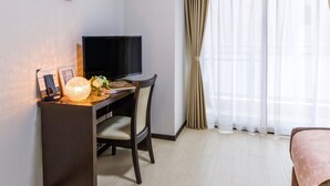 A hotel room with a desk, a television, a bed, and a window with curtains. - Mr.KINJO in MATSUYAMA (Naha)