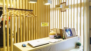 A reception desk with a laptop, a mouse, a lamp, and a small plant. There are wooden slats in the background and a sign with Japanese text. - Mr.KINJO in MATSUYAMA (Naha)