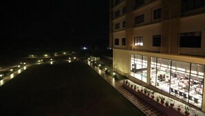 A hotel with a spacious outdoor area, a well-lit dining area, and a checkered pathway with potted plants.
