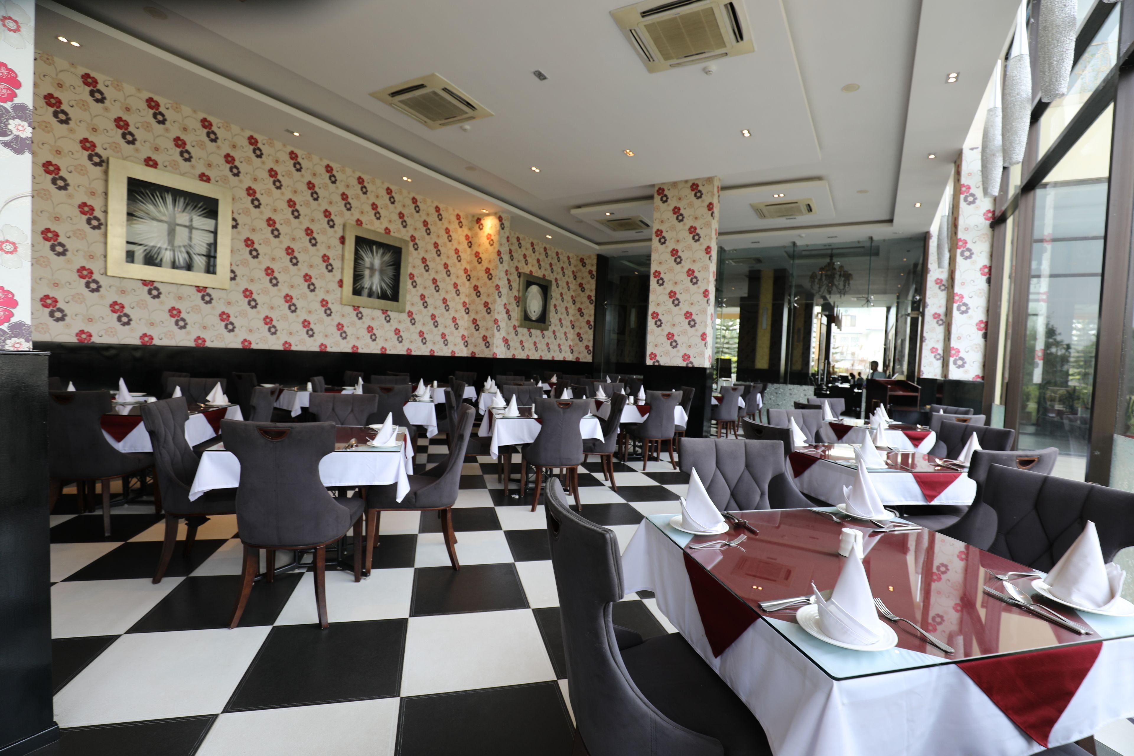 Een restaurant met een schakeerd vloer, tafels met witte tafellinnen en grijze gestoffeerde zitbanken.