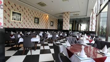 Een restaurant met een schakeerd vloer, tafels met witte tafellinnen en grijze gestoffeerde zitbanken.