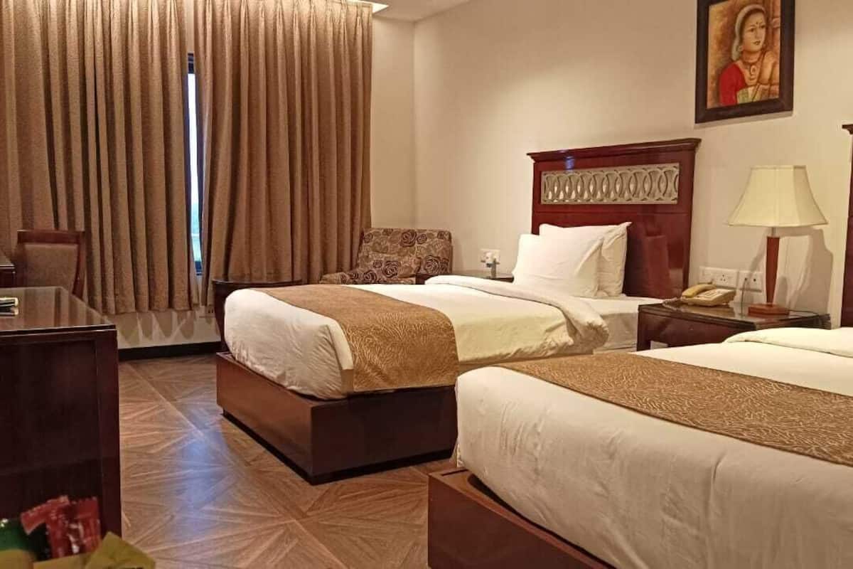 A hotel room with two beds, a desk, a chair, a TV, and a window with curtains.