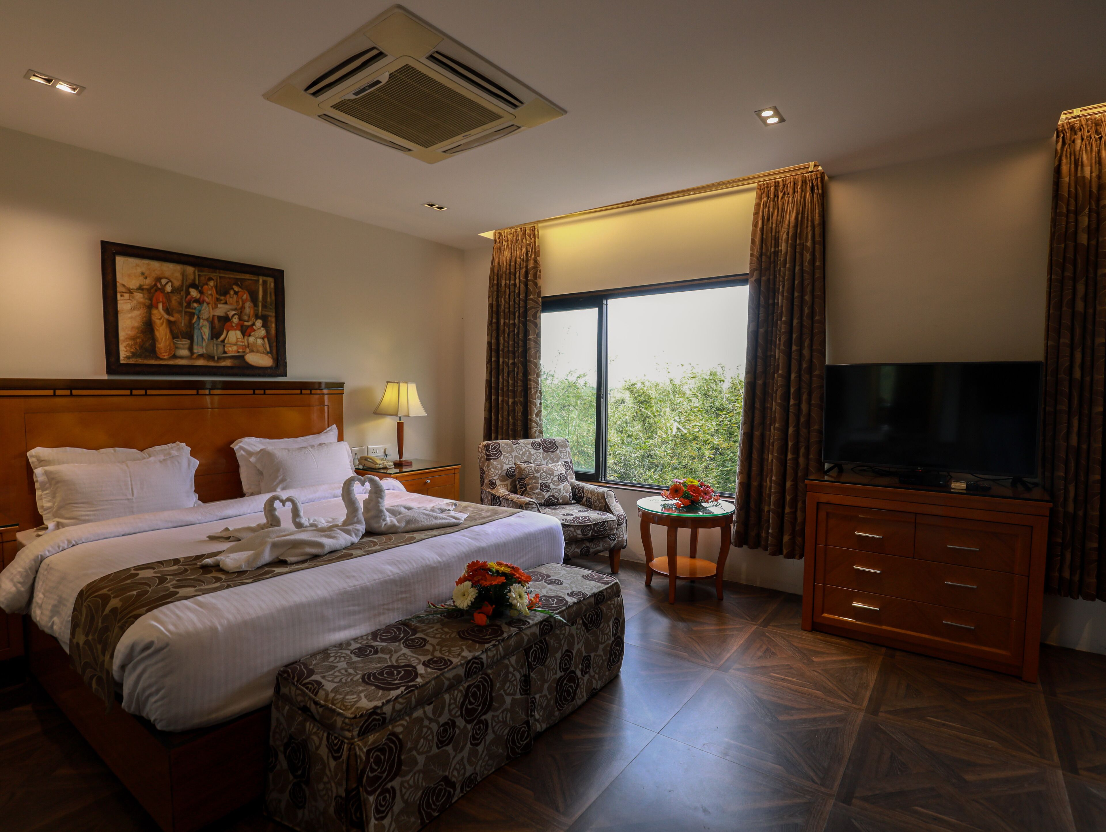 A hotel room with a bed, a TV, a chair, a small table, and a window with curtains.