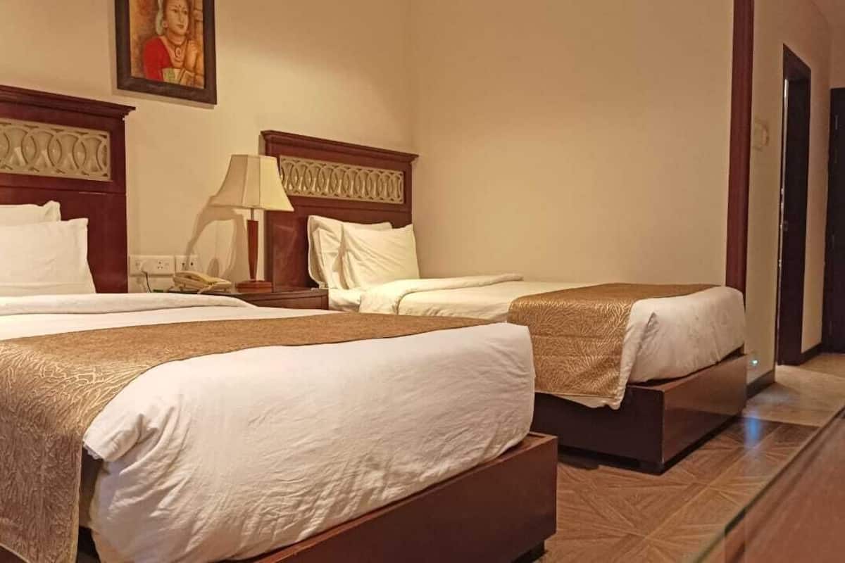 A hotel room with two beds, a nightstand, a lamp, and a painting on the wall.