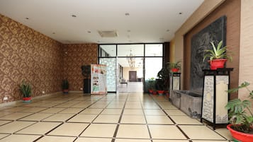 A spacious lobby with patterned walls, tiled flooring, and potted plants.