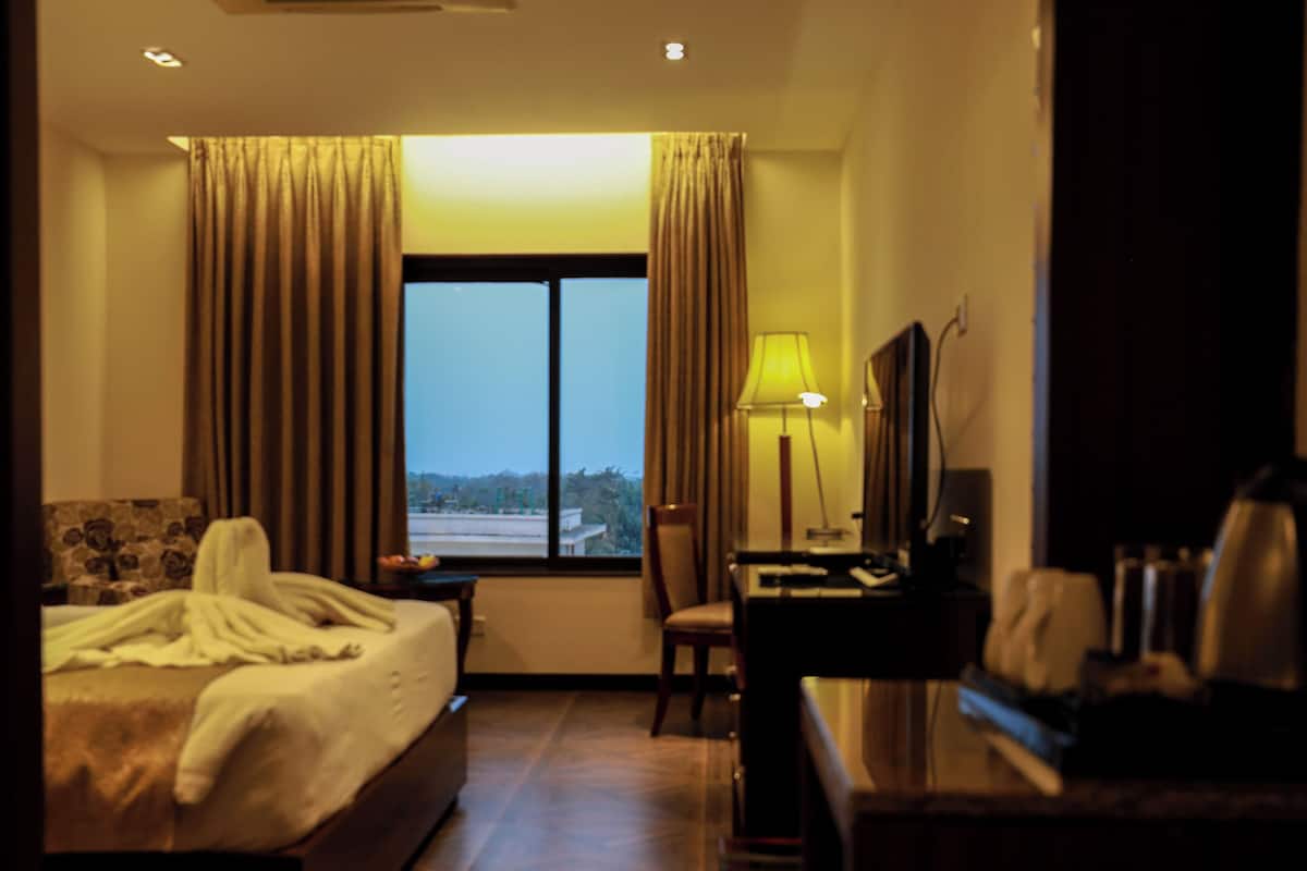 A hotel room with a bed, a desk, a chair, a TV, and a window with curtains.