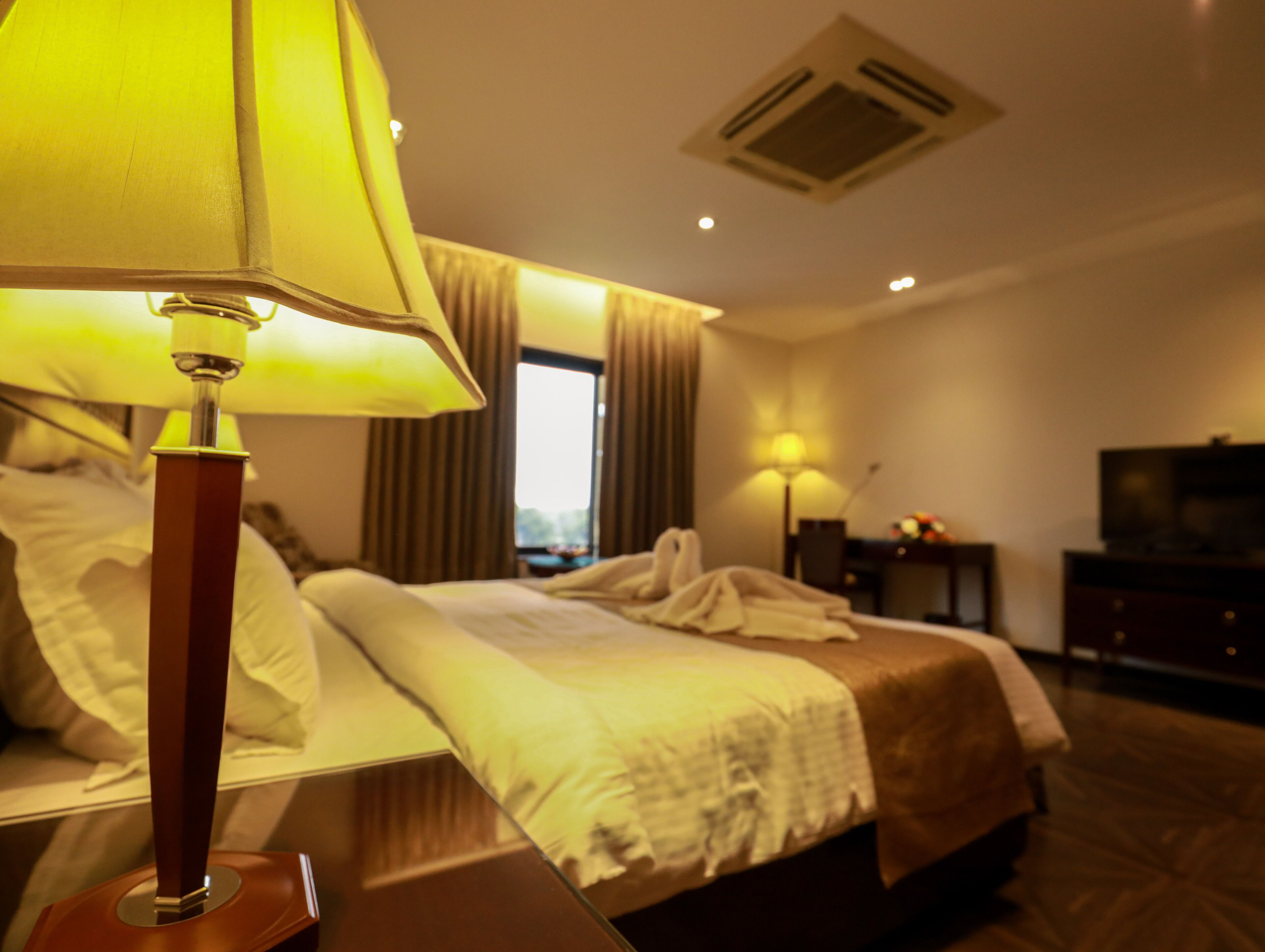 A hotel room with a bed, a bedside lamp, a TV, and a window with curtains.