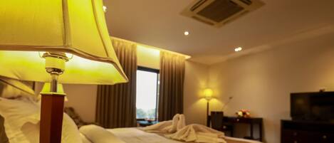 A hotel room with a bed, a bedside lamp, a TV, and a window with curtains.
