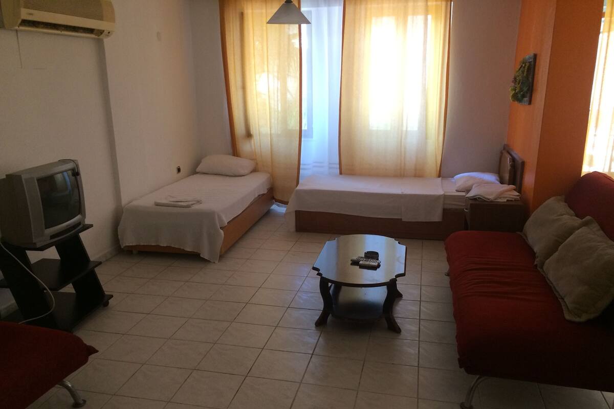 A small, well-lit room with two beds, a TV, a red sofa, and a coffee table.