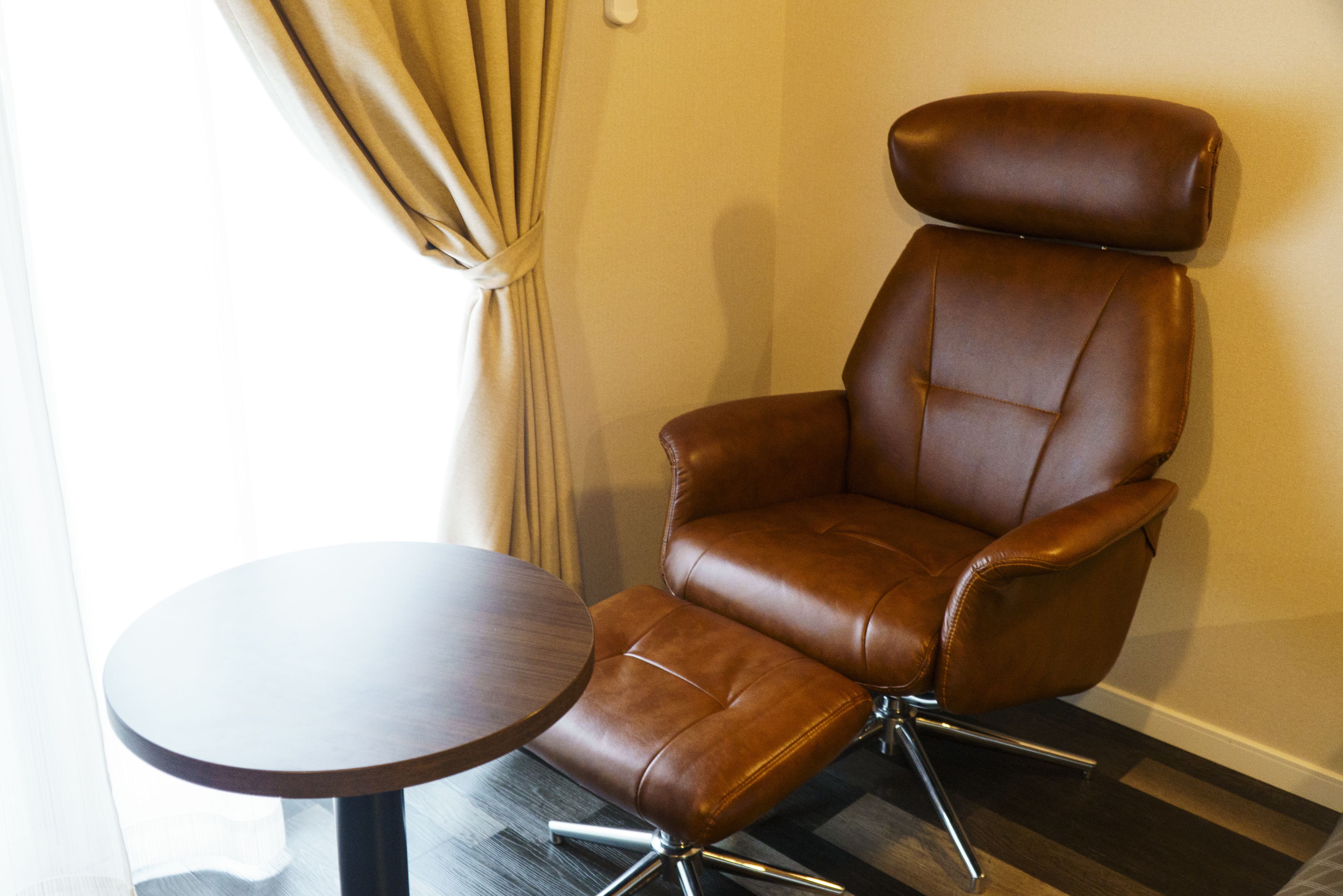 A brown leather armchair with a high backrest and a small round table beside it.