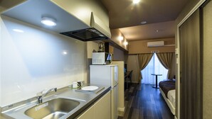 A compact hotel room with a kitchenette, a bed, a small table, and a window with curtains. - Mr.KINJO in Asahibashi station square (Naha)