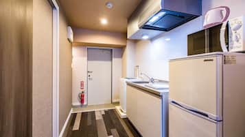 Een kleine keuken met een magnetron, spoelbak en koelkast, een brandblusser, en een deur naar een andere kamer.