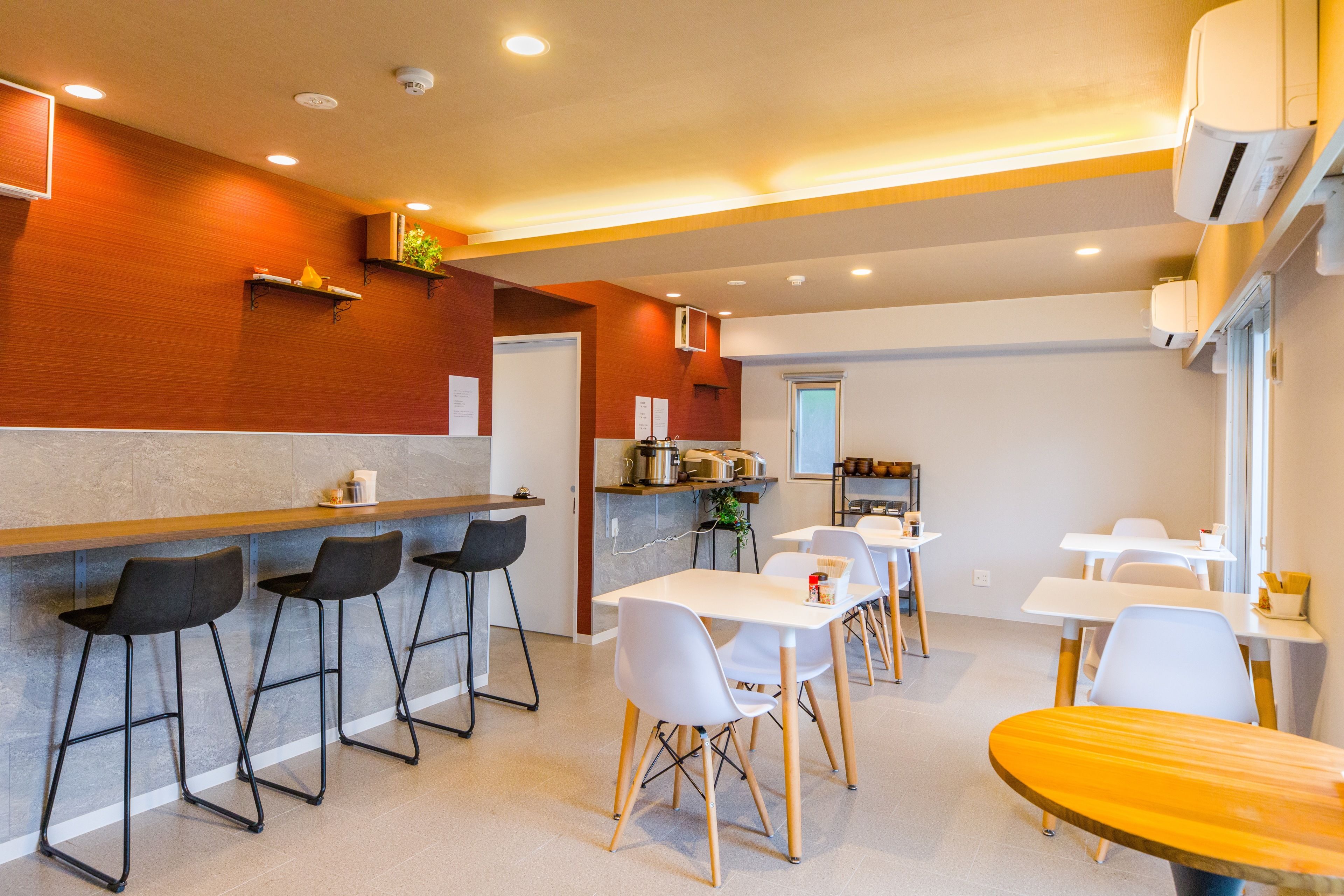 A modern restaurant with a bar area, white tables, and black bar stools.