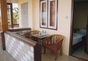 A small dining area with a brick wall, wooden chairs, a table with a tray of items, and a bed in the background. - Pekon Princess Resort (Pekon)