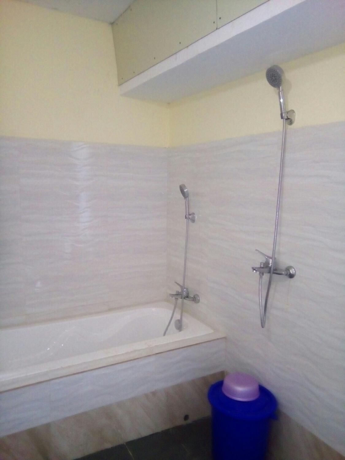 A bathroom with a bathtub, a shower, and a blue trash bin.