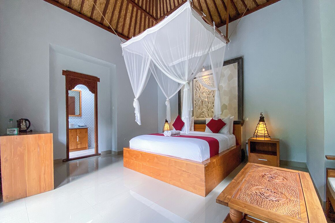 Un dormitorio con una cama de madera, ropa de cama blanca, dosel, mesita de noche con lámpara y una mesa de madera.