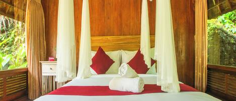 A four-poster canopy bed with a wooden headboard, red and white pillows, and a rolled white towel on the bed.