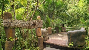 A rustic wooden sign with the text "BALI MUTUAUNIK" and a stone bench in a lush, green garden setting. - Bali Jungle Resort (Sebatu)