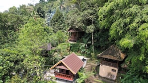 A remote, rustic lodge nestled in a lush forest, featuring a main building with a red roof and a smaller structure with a thatched roof. - Bali Jungle Resort (Sebatu)