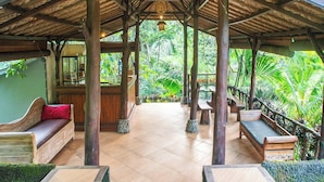 A covered outdoor seating area with wooden benches and a tiled floor, surrounded by lush greenery. - Bali Jungle Resort (Sebatu)
