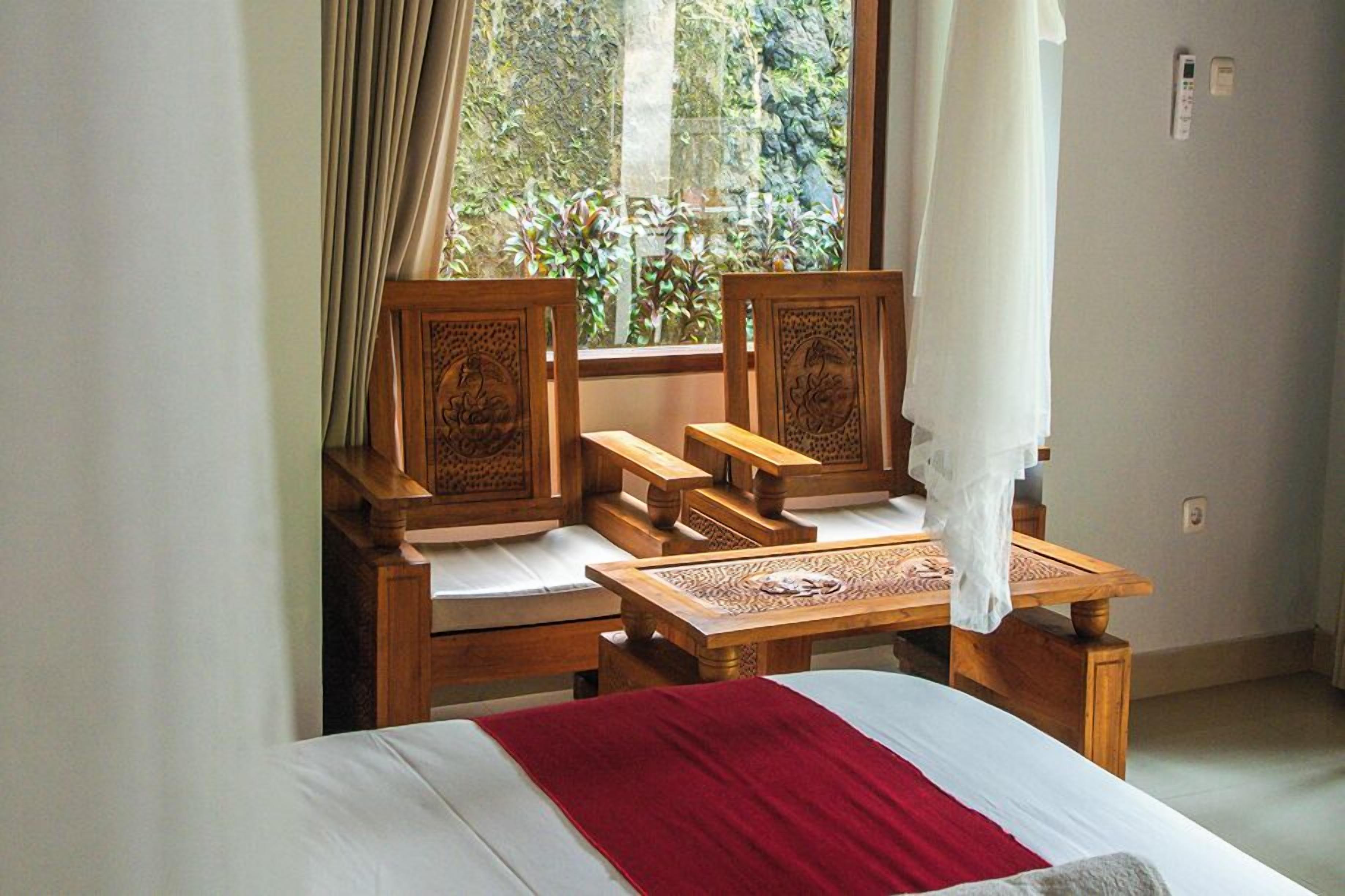 Una habitación con cama, sillas de madera, una mesita y un ventanal con cortinas.