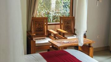Una habitación con cama, sillas de madera, una mesita y un ventanal con cortinas.