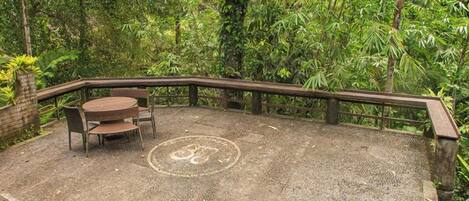 An outdoor seating area with a round table and chairs, surrounded by a wooden fence and dense foliage.