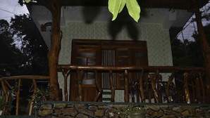 Estructura de madera tradicional con un muro de piedra frontal, que presenta una puerta de madera y un balcón con barandilla.