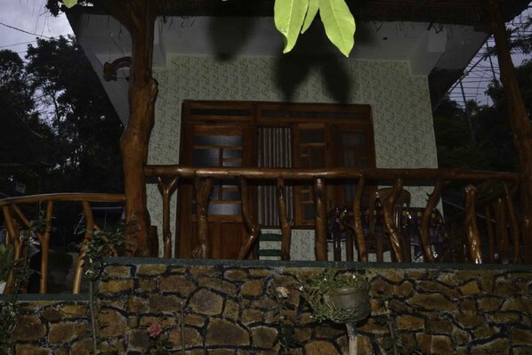 A traditional wooden structure with a stone wall in front, featuring a wooden door and a balcony with a railing.