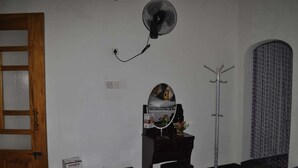 Una habitación con puerta de madera, un ventilador de pie, perchero y una mesita con una caja y pañuelos.