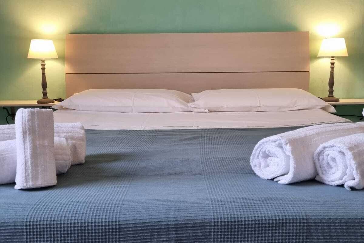 A neatly made bed with white linens, two bedside lamps, and rolled towels on the bed.