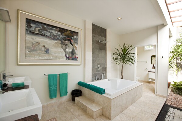 A modern bathroom with a large bathtub, a sink, and a shower area. There is a framed painting on the wall and a potted plant in the corner. - The Villas by Puri Mas Boutique Resort (Senggigi)