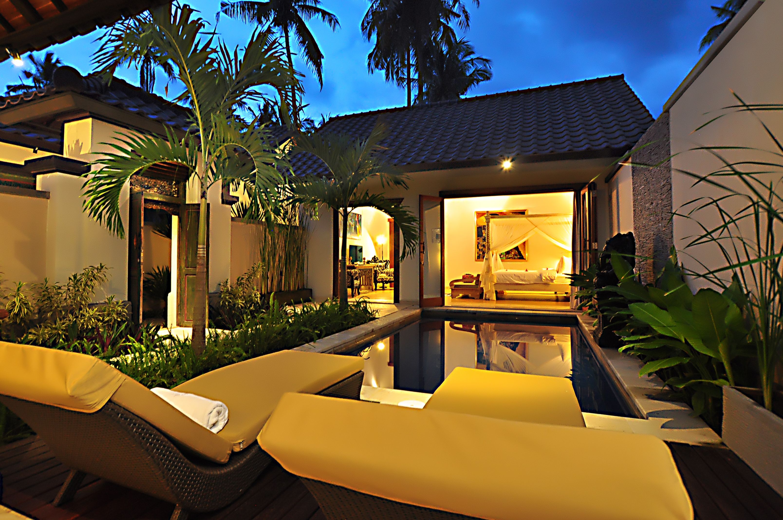 Zona junto a la piscina con sillones, una piscina pequeña y un espacio interior bien iluminado con cama y zona de estar.