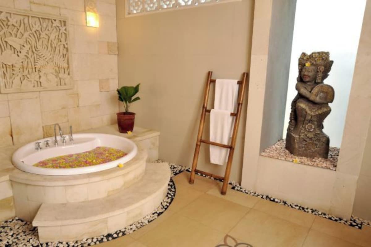 A bathroom with a freestanding bathtub, a wooden ladder, a statue, and a decorative wall panel.