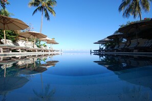 Ein Poolbereich mit Liegestühlen und Sonnenschirmen, Palmen und freiem Blick auf den Ozean.