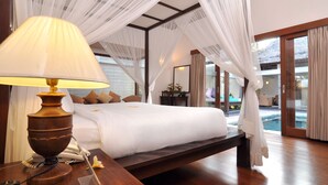 Ein Hotelzimmer mit Bett, Nachttischlampe, Telefon und Blick auf einen Pool durch große Fenster.