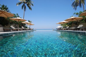A clear pool with lounge chairs and umbrellas, palm trees, and a view of the ocean. - The Villas by Puri Mas Boutique Resort (Senggigi)