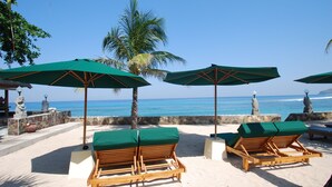 Ein Strandloungebereich mit Holzliegen und grünen Sonnenschirmen mit Blick aufs Meer.