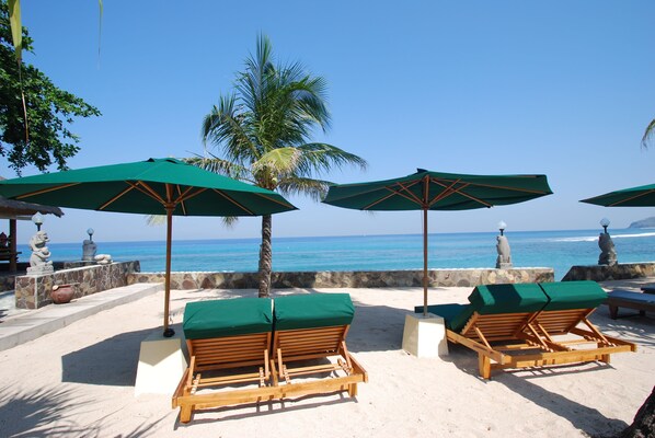 Ein Strandloungebereich mit Holzliegen und grünen Sonnenschirmen mit Blick aufs Meer.