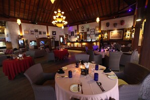 Ein Restaurant mit runden Tischen, Korbstühlen und einer Bar.