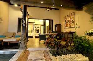 A room with a bed, a statue, a dining area, and a painting on the wall. - The Villas by Puri Mas Boutique Resort (Senggigi)