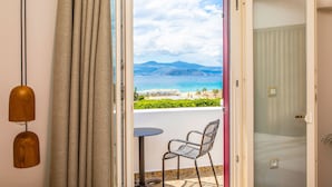 A room with a view of a beach and mountains, a small table, a chair, and a curtain. - Ariadne Hotel (Naxos)