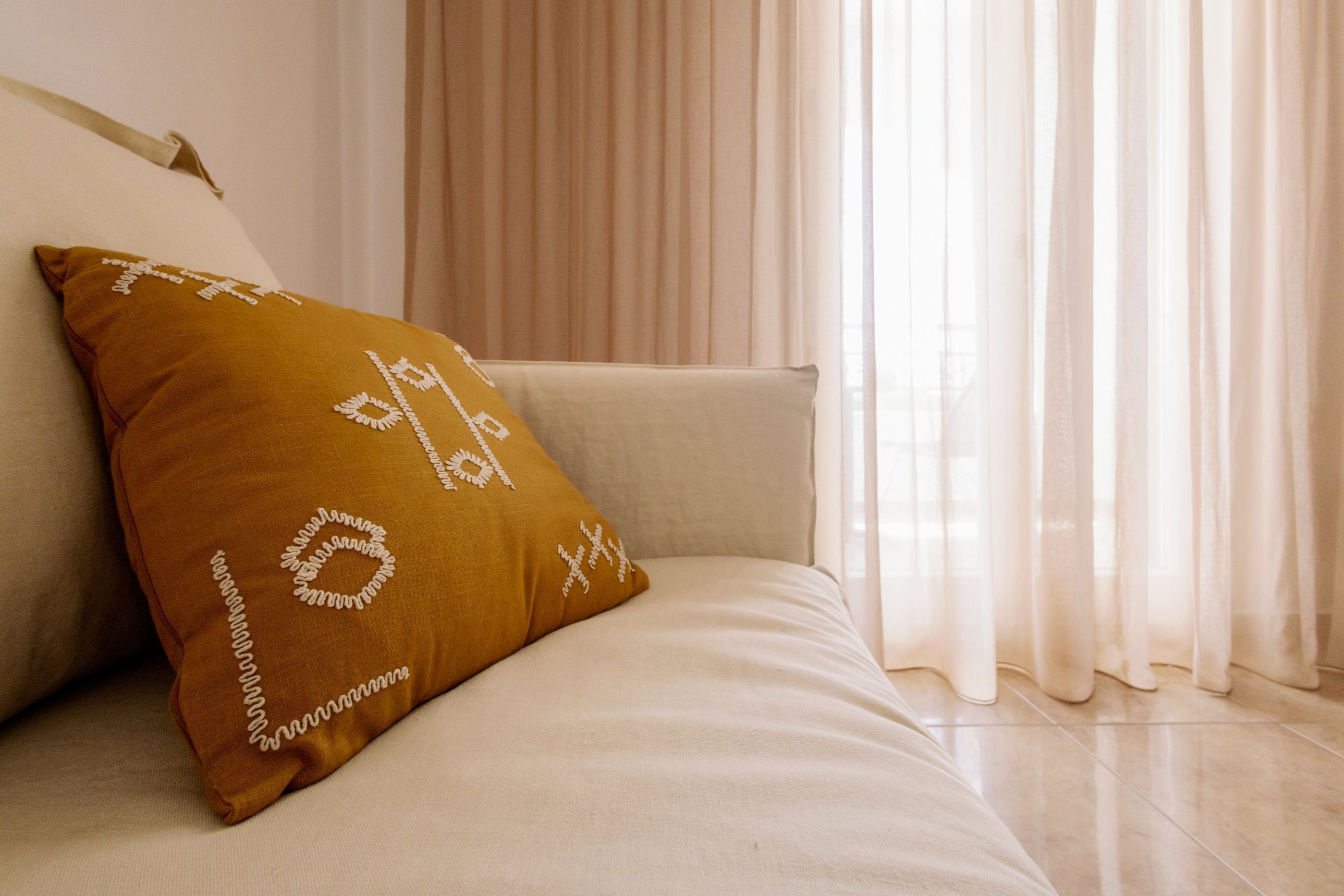 Una cama bien tendida con una sola almohada marrón y una manta color beige.
