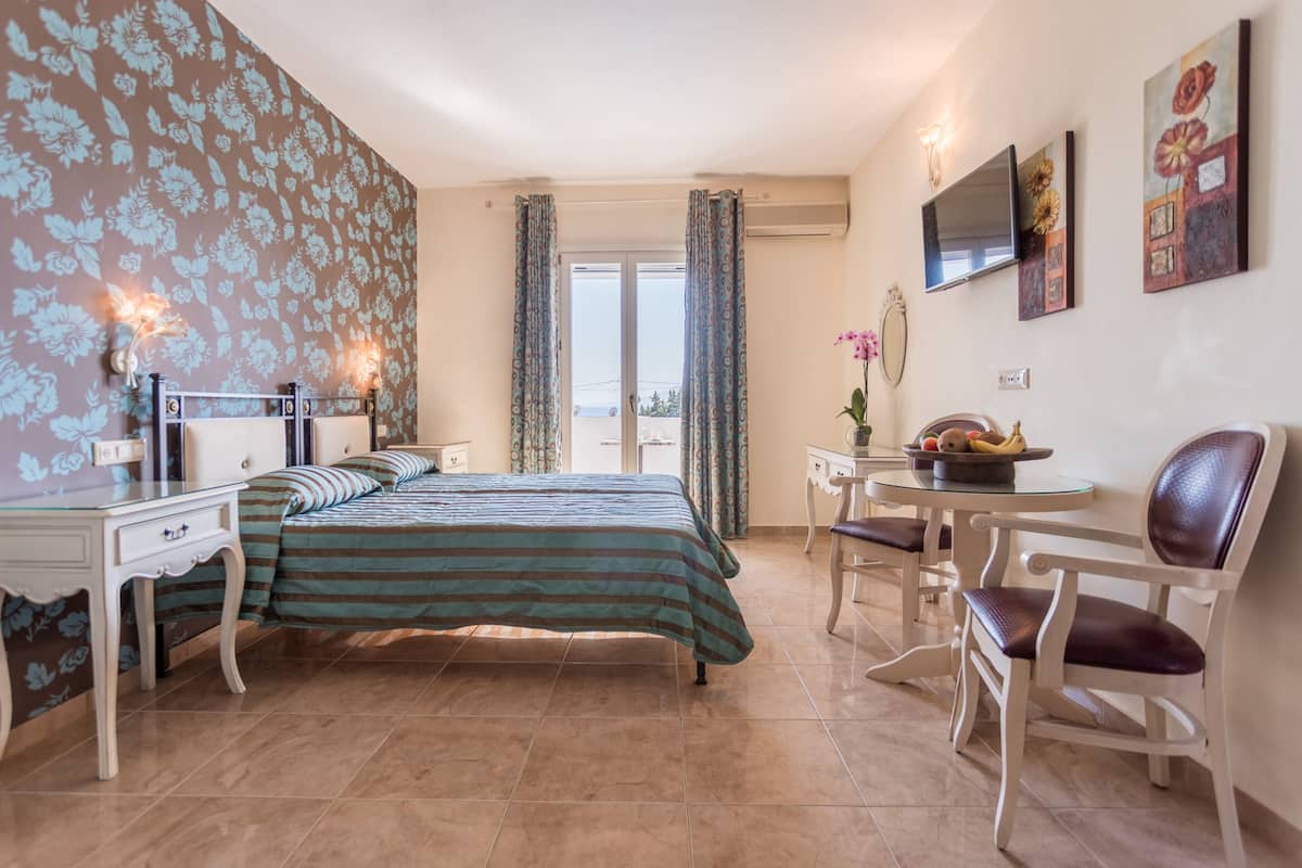 Habitación de hotel con cama, escritorio, silla, una mesita y vistas al balcón.