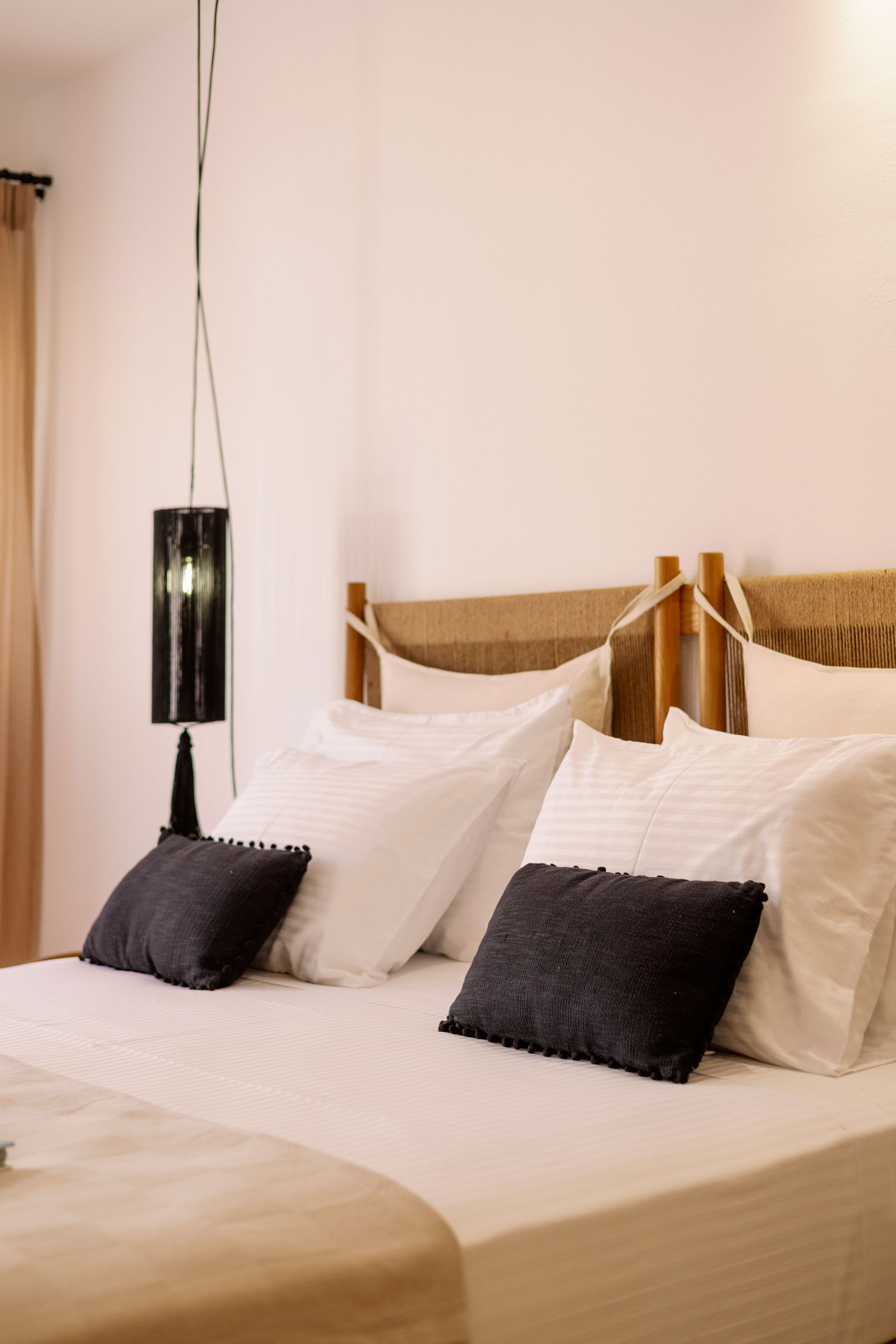 A neatly made bed with white and dark pillows, a wooden headboard, and a black lamp on the nightstand.