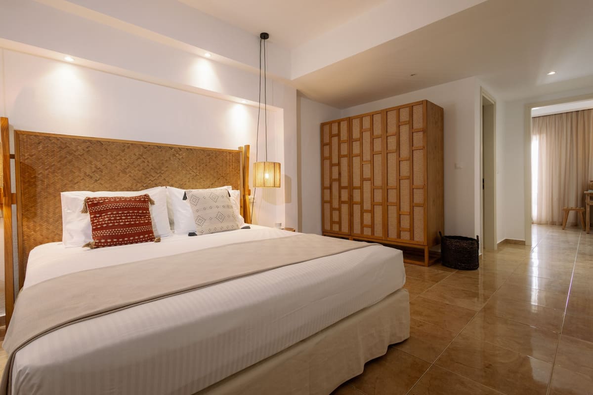 Una cama grande con cabecera de madera, una lámpara de noche y un separador tejido.