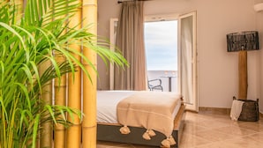 A hotel room with a bed, a view of the sea, a bamboo plant, and a lamp. - Ariadne Hotel (Naxos)