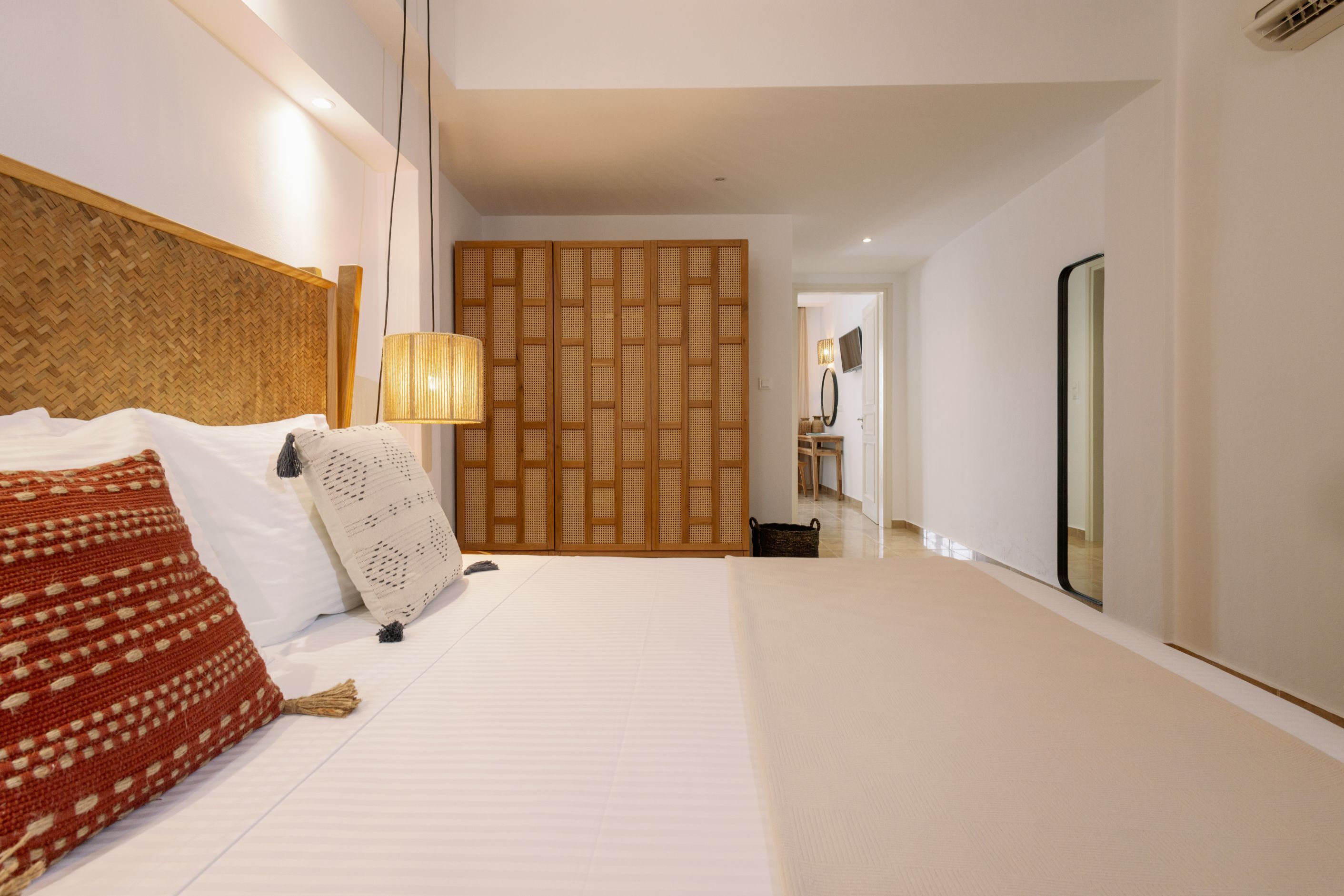 A hotel room with a large bed, a wooden headboard, a woven partition, a bedside lamp, and a large mirror.